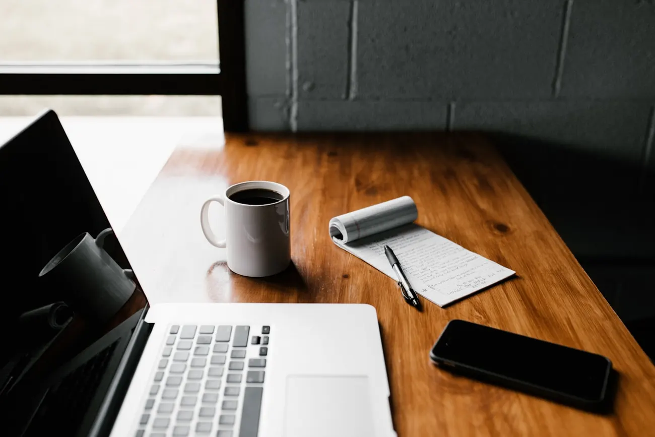 A wooden desk with a laptop, coffee, and a handwritten notepad — the raw material of a discovery call.